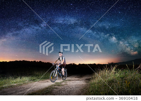 Cyclist riding bike in the night under starry sky Cyclist riding bike in the night under starry sky 36910418