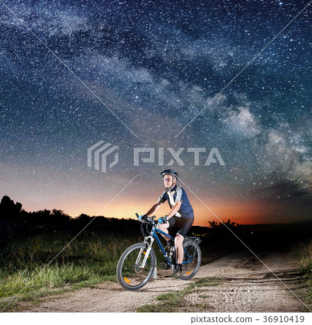 Cyclist riding bike in the night under starry sky Cyclist riding bike in the night under starry sky 36910419
