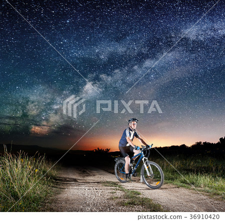 Cyclist riding bike in the night under starry sky Cyclist riding bike in the night under starry sky 36910420