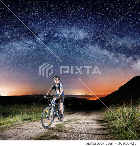 Cyclist riding bike in the night under starry sky Cyclist riding bike in the night under starry sky 36910425