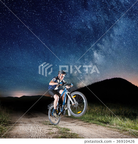 Cyclist riding bike in the night under starry sky Cyclist riding bike in the night under starry sky 36910426
