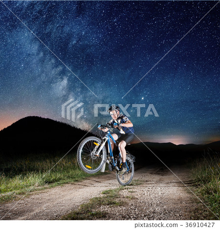 Cyclist riding bike in the night under starry sky 36910427