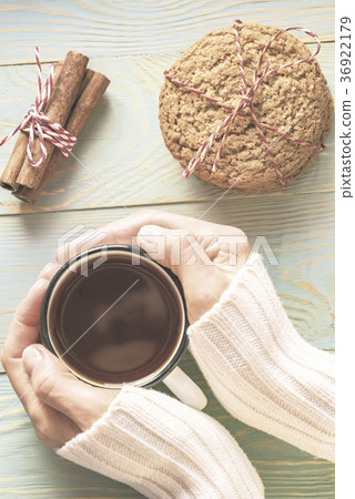 Woman in sweater holds cup of tea on wooden table Woman in sweater holds cup of tea on wooden table 36922179
