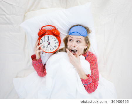Shocked woman wearing pajamas holding clock overslept Shocked woman wearing pajamas holding clock overslept 36980465
