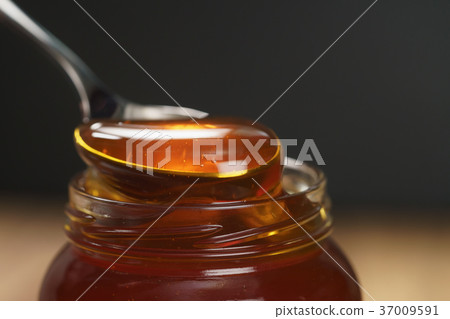 scooping organic honey with spoon from glass jar scooping organic honey with spoon from glass jar 37009591