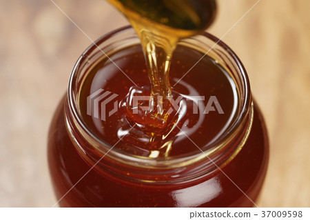pouring organic honey from spoon into glass jar pouring organic honey from spoon into glass jar 37009598
