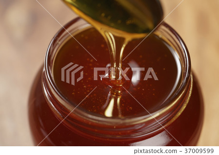 pouring organic honey from spoon into glass jar pouring organic honey from spoon into glass jar 37009599