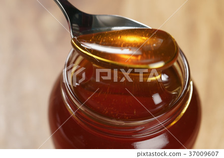 scooping organic honey with spoon from glass jar scooping organic honey with spoon from glass jar 37009607