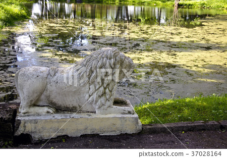Ancient lion sculpture near old pond in park 37028164