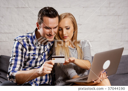 young man and woman are sitting on the couch and they are shopping online 37044190