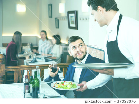Waiter serving delicious salads to handsome young man at restaurant 37058070