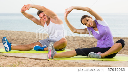 Young smiling couple doing yoga poses sitting on sunny beach 37059083