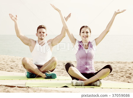 Cross-legged couple practice yoga on beach in morning 37059086