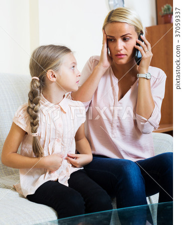 Worried mother calling doctor for daughter with abdominal pains Worried mother calling doctor for daughter with abdominal pains 37059337