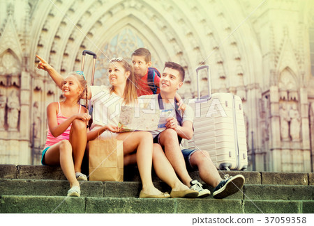 Family of four relaxing on old cathedral steps looking map Family of four relaxing on old cathedral steps looking map 37059358