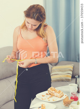 sad female making measurement after eating cake sad female making measurement after eating cake 37059433