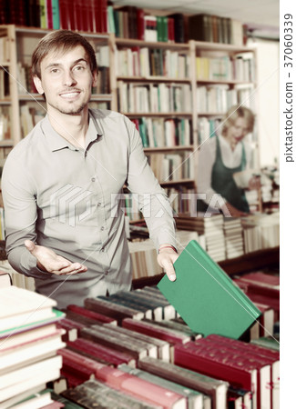 Positive man customer looking for new book on shelves 37060339