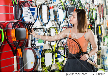 Girl standing in t-shirt in sporting goods store with racket 37060904