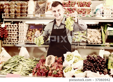 positive male seller showing assortment of grocery shop 37060942