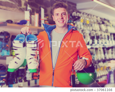 Adult man in jacket and helmet is demonstrating his choice of boots for skiing. 37061108