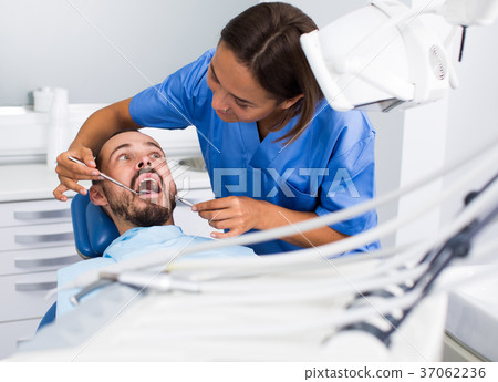 Dentist female in uniform is examinating of male in dental clinic Dentist female in uniform is examinating of male in dental clinic 37062236