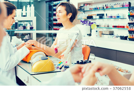 attentive female manicurist filing and shaping nails in beauty salon 37062558