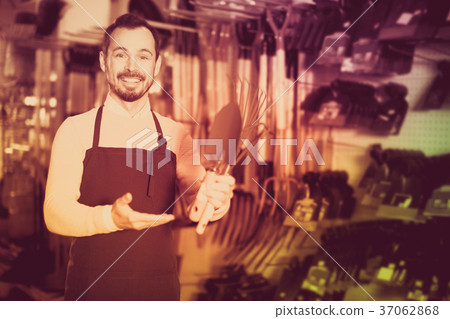 Seller displaying various items in garden equipment shop Seller displaying various items in garden equipment shop 37062868