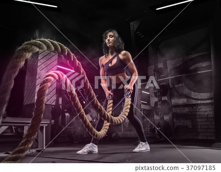 In a modern gym, a young girl is engaged in fitness using a rope 37097185