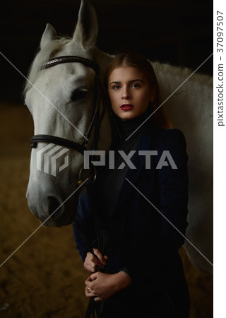 Serious blonde in blue jacket stands with a horse. 37097507