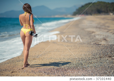 Naked woman in the bikini with camera on the sand Naked woman in the bikini with camera on the sand 37101440