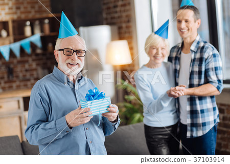 Pleasant elderly man posing with a present for his Pleasant elderly man posing with a present for his 37103914