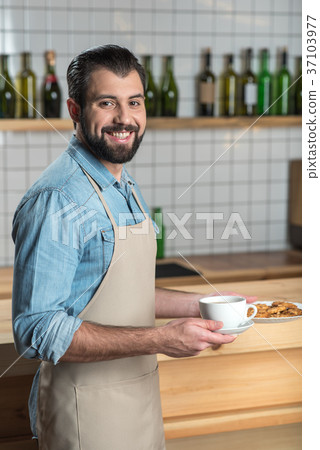 Handsome friendly waiter smiling while holding a Handsome friendly waiter smiling while holding a 37103977