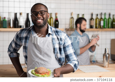 Cheerful handsome waiter standing with a tasty 37104118