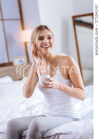 Cheerful woman touching her face while holding 37104242