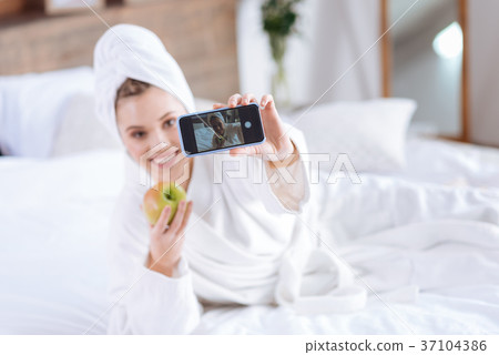 Joyful woman taking selfie with apple on bed 37104386