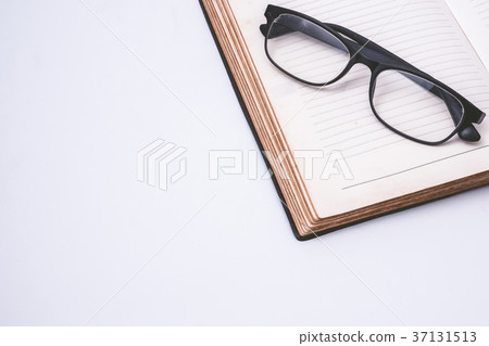An open notebook with glasses on white background. 37131513