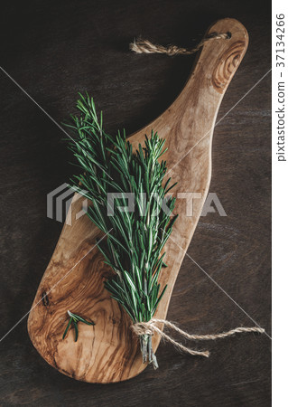 The branch of fresh rosemary on the rustic board The branch of fresh rosemary on the rustic board 37134266
