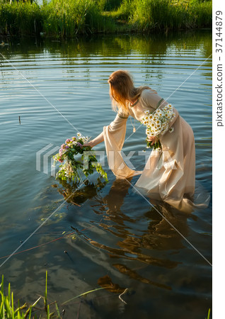 Attractive woman lowers wreath in water 37144879