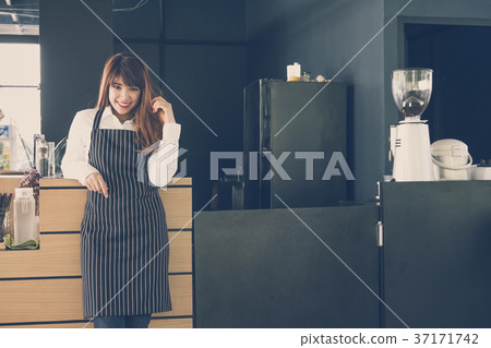 small business owner standing at counter in coffee shop. female barista wearing apron smiling at bar in cafe. food service, restaurant concept. 37171742
