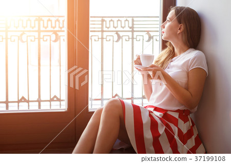 Young woman drinking coffee sitting near balcony 37199108