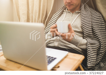 Young man laying in bad with laptop and cup of tea Young man laying in bad with laptop and cup of tea 37224027