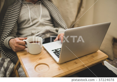 Young man laying in bad with laptop and cup of tea Young man laying in bad with laptop and cup of tea 37224078