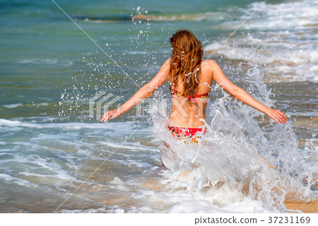 Beautiful young woman sits on sand of beach 37231169