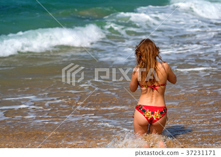 Beautiful young woman sits on sand of beach 37231171