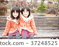 Twin sisters sitting on a bench 37248525
