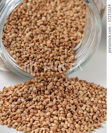 Uncooked buckwheat scattered from jar on table Uncooked buckwheat scattered from jar on table 37251024