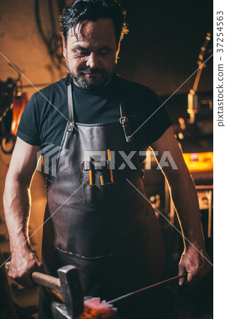 Senior blacksmith forging molten metal on the 37254563