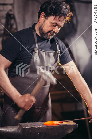 Blacksmith forging molten metal on the anvil in 37254581