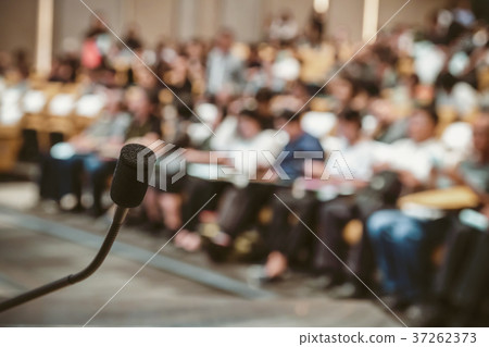 Microphone over the Abstract blurred photo of conference hall or seminar room with attendee background Microphone over the Abstract blurred photo of conference hall or seminar room with attendee background 37262373