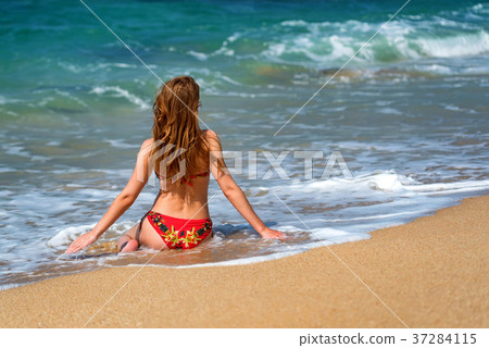 Beautiful young woman sits on sand of beach 37284115